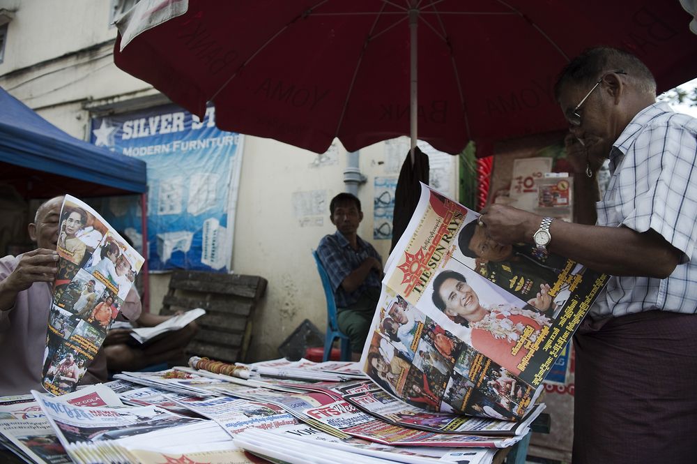A man (R) reads a newspaper featuring a special election double spread front and back page featuring pictures of Myanmar opposition leader Aung San Suu Kyi, Myanmar's army chief General Min Aung Hlaing, Myanmar's President Thein Sein and various election supporters moments, in Yangon on November 7, 2015. The once junta-run nation heads to the polls on November 8 in what voters and observers hope will be the freest election in decades. While NLD party is expected to triumph at key elections this year, Myanmar opposition leader Aung San Suu Kyi's pathway to the presidency is blocked by a controversial clause in Myanmar's junta-era constitution. AFP PHOTO / Nicolas ASFOURI