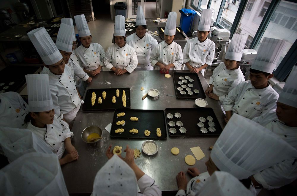 This picture taken on December 1, 2015 shows students of the Shanghai Young Bakers listening to their teacher during a bakery training class in Shanghai. The Shanghai Young Bakers NGO offers a one year vocational training course for Chinese youth who have family difficulties resulting in them having to drop out of school because of financial problems or parental health issues. This year's 31 students who come from all over China are trained in French baking as well as English language skills. The students spend one week in school and the other week as an intern in different international hotels in Shanghai. AFP PHOTO / JOHANNES EISELE