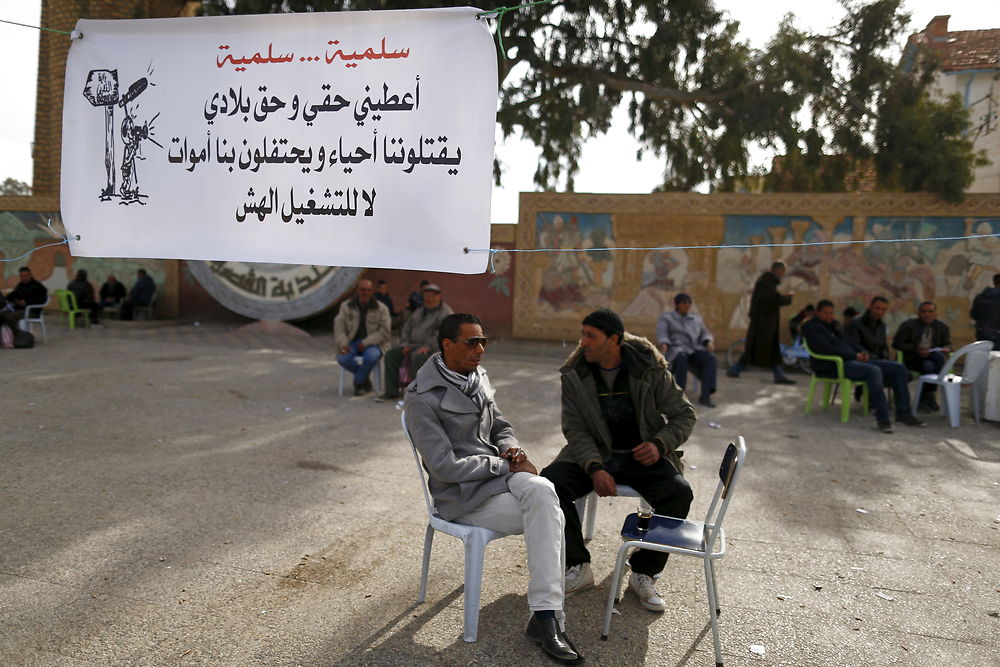 Arbejdsløse sidde på en cafe i Kasserine. På skiltet står der: »Giv mig og mit land vores rettigheder. De begraver os levende og danser på vores grav. Nej til arbejdsløsheden.«