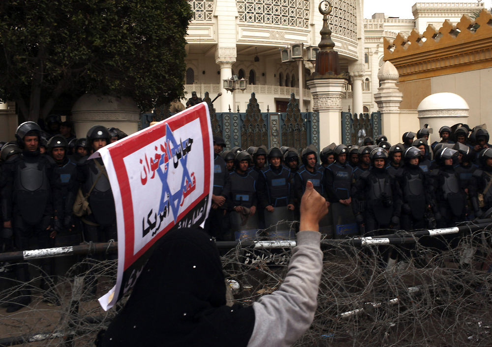 A protester carries a sign as she gestures during a protest against Egyptian President Mohammed Mursi in front of the presidential palace, in Cairo in this February 1, 2013 file photo. In Egypt, Libya and Syria, where Qatar tried to play a role post-Arab Spring, it finds itself blamed for much that has gone wrong on a local level. Close ties to Egypt's new leaders, the Muslim Brotherhood, have alarmed countries like the United Arab Emirates, where the Islamist group is still banned and which in January said it had foiled a Brotherhood-linked coup plot. The sign reads, "Hamas, Qatar, the Muslim Brotherhood and the U.S. are the enemies of Egypt". To match QATAR-NEIGHBOURS/ REUTERS/Asmaa Waguih/Files (EGYPT - Tags: POLITICS CIVIL UNREST)