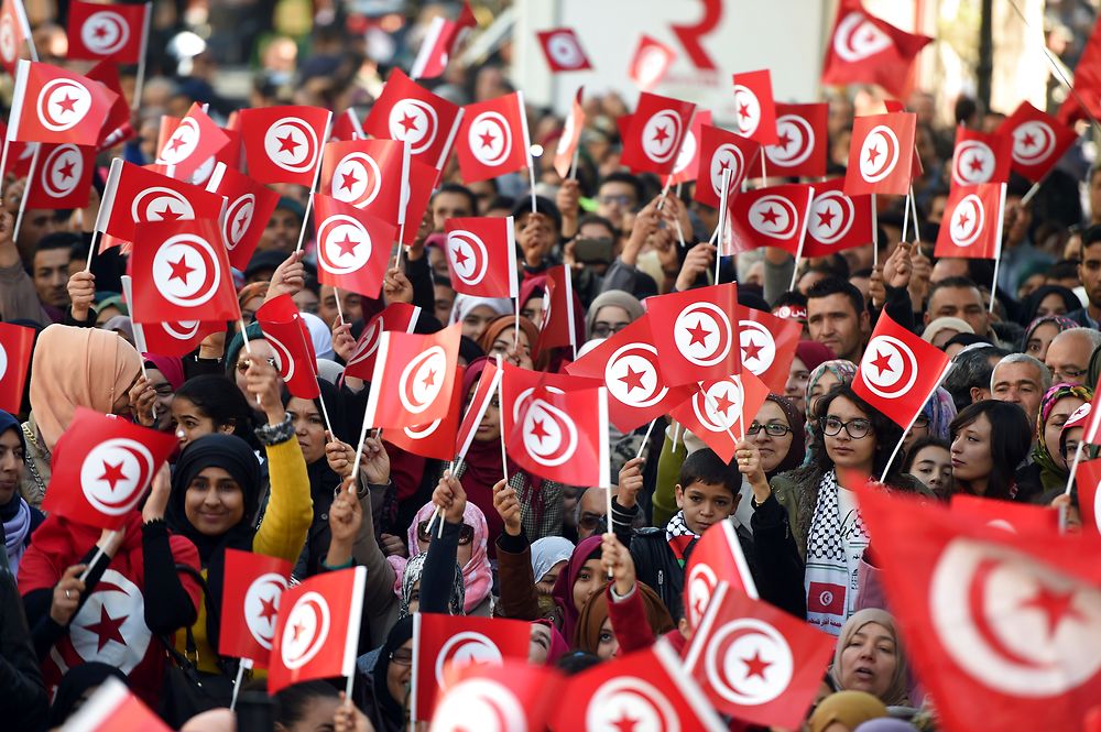 TOPSHOT - Tunisians wave national flags and shout slogans on January 14, 2016, during a rally on Habib Bourguiba Avenue in Tunis to mark the fifth anniversary of the 2011 revolution. / AFP / FETHI BELAID